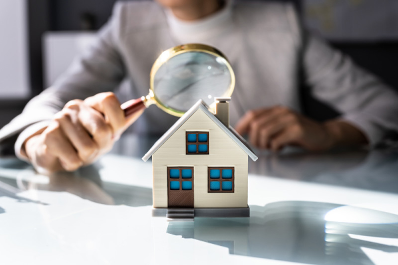 Immobilienmakler Dornbusch hält eine Lupe über ein kleines Haus um Immobilie zu bewerten